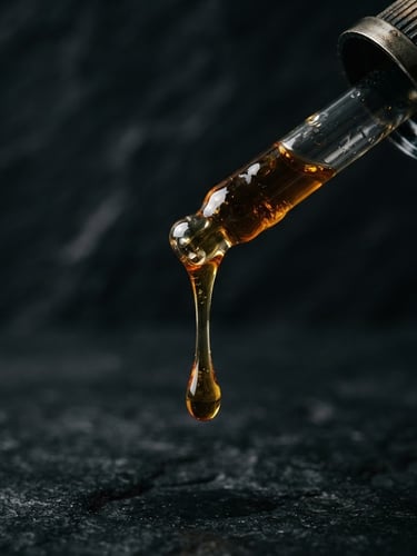 Macro close-up of thick golden oud oil dripping from a glass dropper, dramatic side lighting, dark obsidian background, 35mm