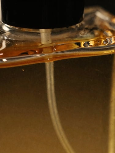 Macro close-up of a heavy crystal perfume bottle being filled with a viscous, golden amber liquid, dramatic low-key lighting, warm side-shadows, 35mm.