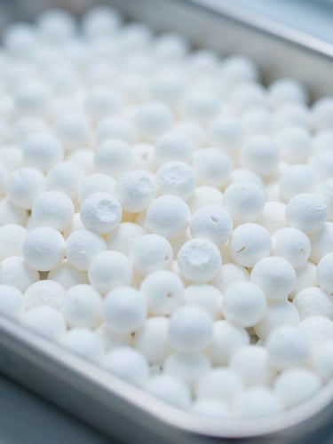 Macro close-up of pure white industrial polymer pellets on a sterile metal tray, bright cool laboratory lighting, shallow depth of field, 35mm