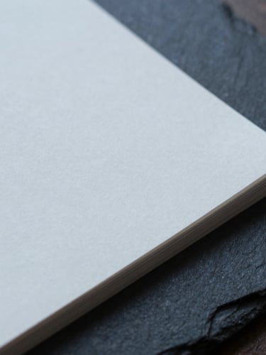 Extreme close-up of heavy cotton paper document on a dark slate desk, sharp focus, cool diffused overcast daylight, desaturated navy tones, 35mm architectural photography style