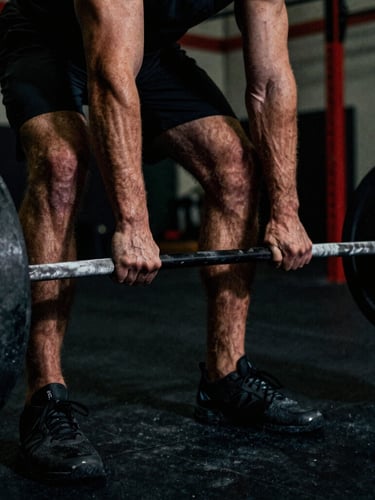 Close-up dramatic low-key shot of a male athlete hands gripping a heavily loaded chalked barbell in a dark warehouse gym, deep shadows, intense physical effort, 35mm film grain