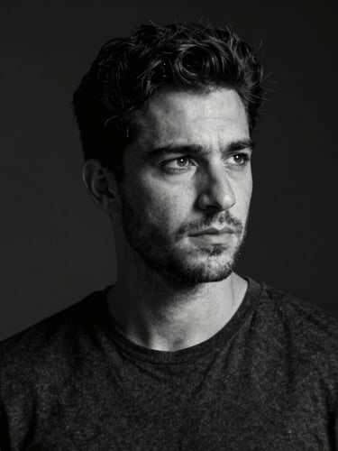 Cinematic, high-contrast black and white portrait of Pablo David Benítez, looking thoughtful, single-source key lighting with deep shadows, dark background.