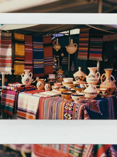 Handmade ceramic pottery and colorful woven textiles displayed at a traditional outdoor market stall.