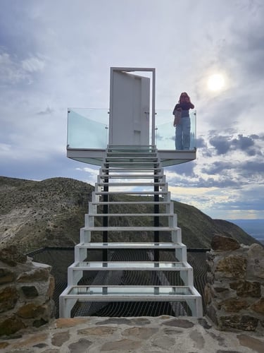 Mujer se encuentra de pie en plataforma de observación, en lo alto de una escaleras que van al cielo