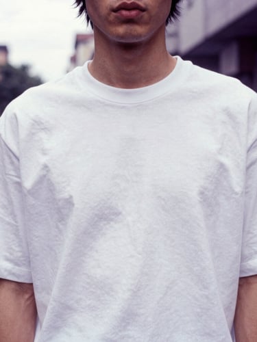 Candid street style portrait of a model from the chest down, wearing a crisp white heavyweight T-shirt, highlighting the thick structural collar and clean shoulder drape, urban background, overcast light