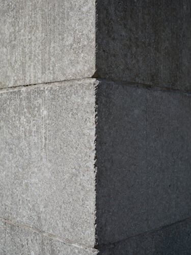 Close detail of a material transition — polished stone meeting raw concrete at a wall junction, diffused daylight raking across the surface, no people, sharp focus on texture and edge precision