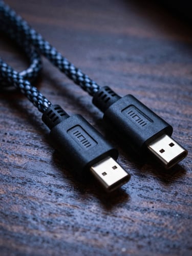 Macro shot of premium braided nylon USB-C cables neatly coiled on a dark wooden desk, high-contrast cool tones