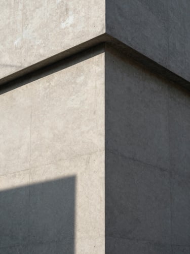 Stark architectural corner of a concrete building, sharp geometric shadow cast by midday sun on a textured wall, minimalist composition, clean lines.