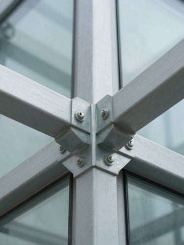 Abstract macro photograph of structured steel joints and architectural glass, clean lines representing structural plumbing, bright daylight, cool tones.