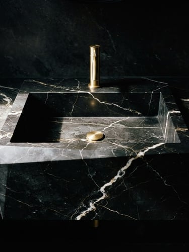 Dramatic architectural photography, close-up of a monolithic black marble washbasin with sharp geometric lines, dramatic side lighting highlighting white veins, 35mm lens