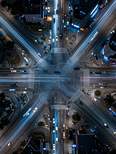 Top-down orthographic aerial view of a complex multi-lane urban intersection at night, sharp neon light trails of moving vehicles, cool blue street illumination, high contrast.