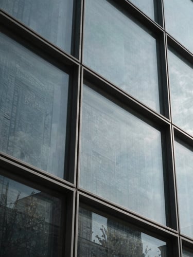 Tight abstract crop of architectural glass and steel angles, cool diffused daylight, sharp high-contrast shadows, 35mm