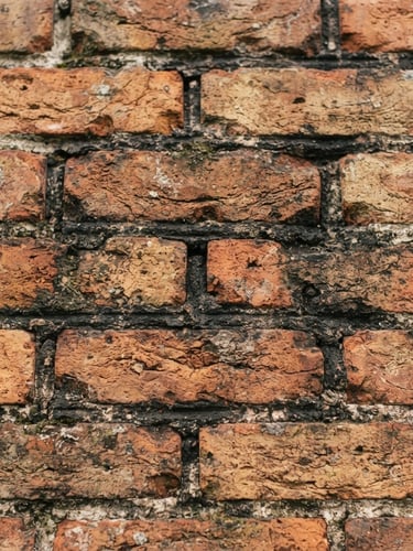 Close-up of weathered brick chimney masonry under a soft New England overcast sky, sharp focus on the mortar joints, warm brick and deep charcoal tones.