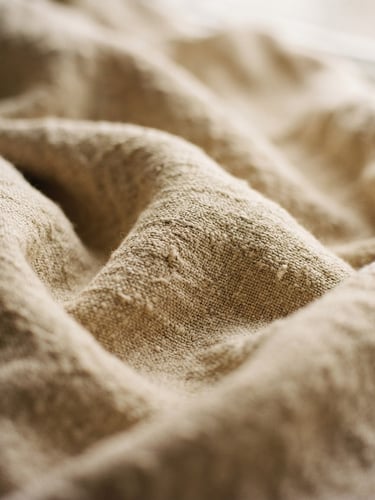 Intimate close-up of draped raw linen fabric in warm sand tones, soft diffused daylight, shallow depth of field, 35mm film