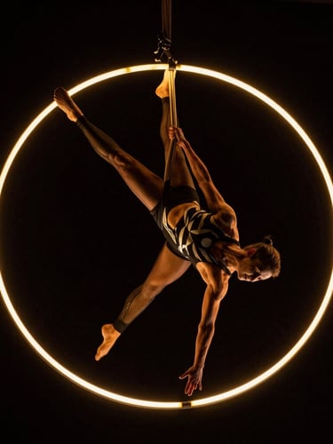 Low-angle dynamic shot of an aerial hoop performer suspended under dramatic golden rim lighting, dark high-contrast theatrical background, 35mm.