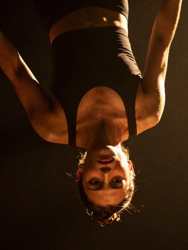 Dramatic close-up of a female aerial hoop artist suspended in mid-air, intense focus on her face, warm golden spotlighting, deep shadows, 35mm cinematic photography.