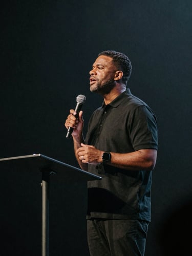 Cinematic editorial photography of a pastor preaching on stage with dramatic side-lighting, deep moody slate tones, shallow depth of field, 35mm film style