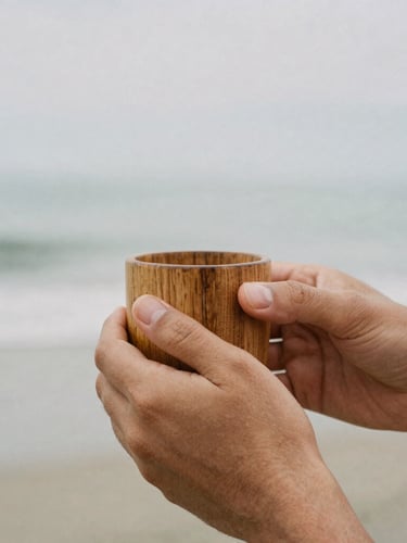 Close-up documentary shot of two hands holding a wooden cup together, soft overcast daylight, muted earth tones, natural 35mm film grain