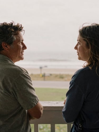 Medium-close environmental portrait of two neighbors talking on a porch in soft overcast daylight, muted earth tones, natural film grain.