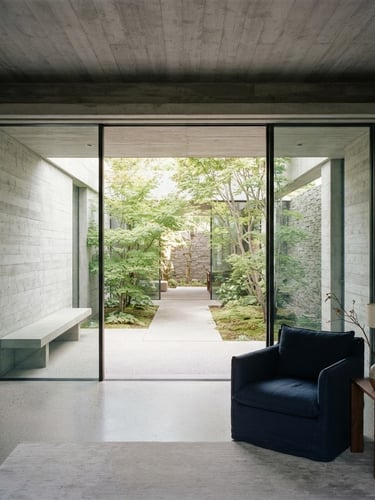 Straight-on architectural photography of a minimalist modern concrete interior with soft diffused daylight, clean shadows, showing a glimpse of a quiet courtyard
