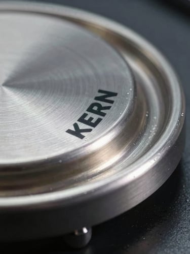 Macro close-up of a KERN scale's brushed steel weighing pan, clinical cool lighting with stark highlights emphasizing the metallic texture, dark industrial background, sharp focus on the precision-engineered edge.