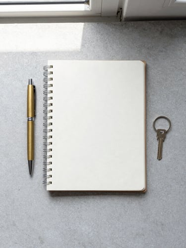A flat-lay of minimalist everyday carry items on a light gray concrete surface, including a clean notebook, a brass pen, and a simple key ring, shot from directly above in soft natural window light.