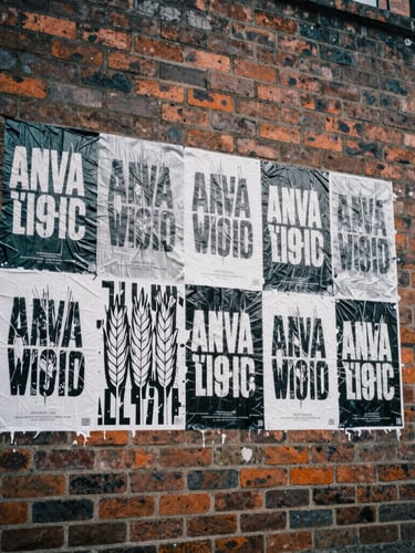 Low-angle street-level shot of a textured brick wall with fresh black and white wheatpasted posters, harsh overcast daylight, gritty film texture.