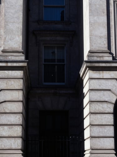 Sharp architectural crop of Regent Street stone facades, high-contrast directional daylight, deep navy shadows, 35mm photography