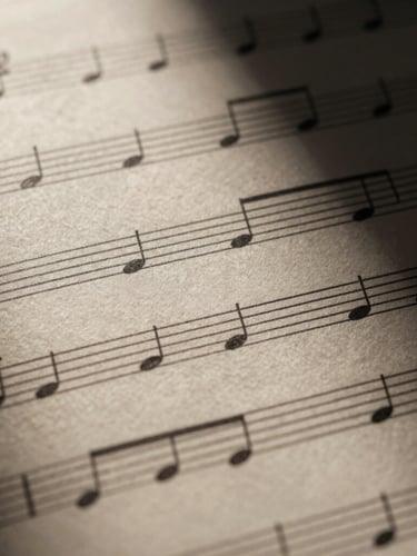 Close-up macro shot of elegant, high-contrast musical notation on thick textured cream paper, dramatic chiaroscuro lighting with deep shadows casting across the staff lines, 35mm anamorphic lens