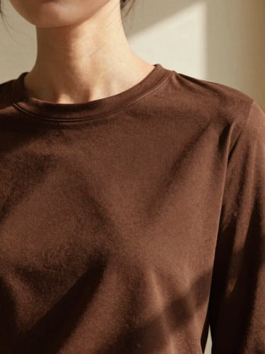 Warm editorial fashion photography of a woman wearing a structured chocolate brown cotton top, soft morning light casting gentle shadows, minimal beige background, 35mm film style.