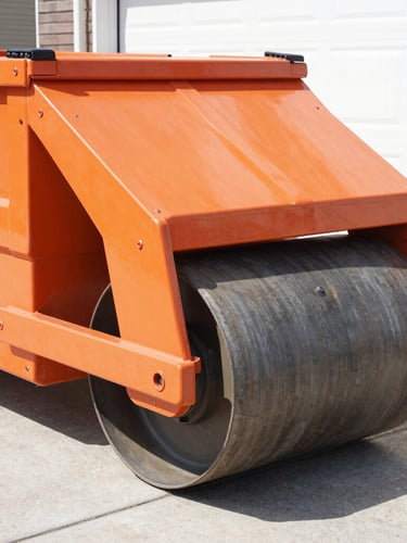 Close-up of heavy-duty steel rollers on a roll-off dumpster, showing the mechanism designed to protect driveways, bright midday sun, crisp industrial photography, orange and charcoal tones, sharp focus.