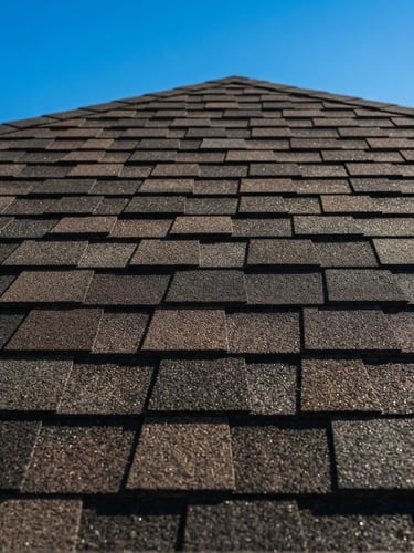 Close-up of clean, new asphalt shingles on a residential roof under bright Texas sunlight, a clear blue sky in the background, showing texture and quality.