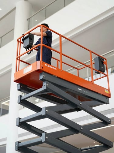 Low-angle side shot of a technician operating the ELEWORK lift inside a bright, modern corporate atrium, hands on the control panel, stable metal structure, clean lines, professional lighting