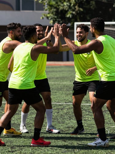 Dynamic action shot of a mixed-gender quadball team huddle on a green field in Lima, high-contrast outdoor daylight, players smiling and high-fiving, 35mm film grain.