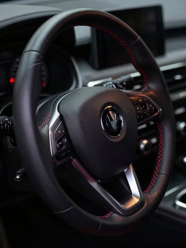 Close-up shot of a pristine, dark leather car interior, focusing on a steering wheel with subtle red stitching, dramatic low-key lighting, sharp details, 35mm lens, bleeding to the left edge.