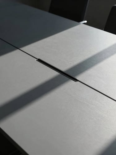 Crisp architectural photography of a minimalist boardroom table with sharp geometric shadows, hard directional daylight, cool gray tones, high contrast