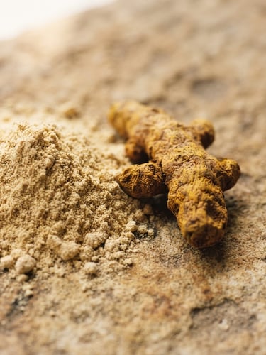 Macro close-up of raw sandalwood powder and turmeric root on a warm textured stone surface, soft morning window light, earthy tones, 35mm
