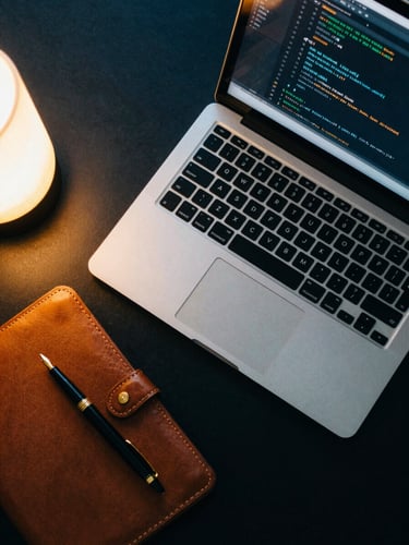 Overhead flat lay of an organized luxury study space, a premium laptop displaying clean code, a gold-capped fountain pen on a leather notebook, warm ambient lighting, 35mm photography