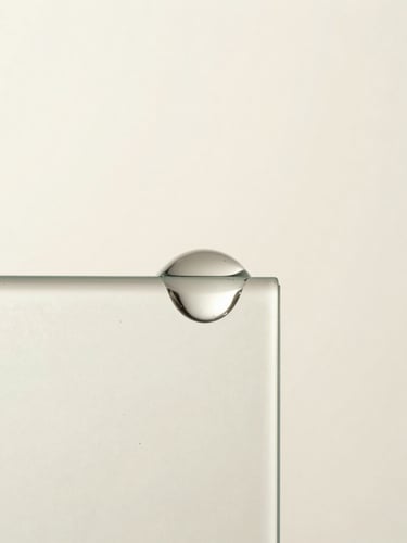 Macro photograph of a single viscous serum droplet suspending on a clean frosted glass edge, soft diffused clinical daylight, sharp focus, minimal composition.
