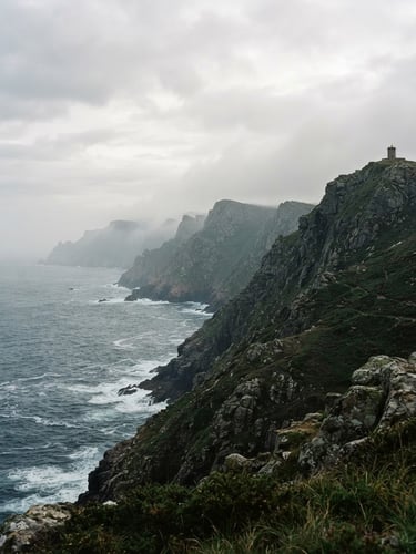 Wide panoramic view of the misty cliffs of Herbeira, Galicia, at soft overcast daylight. The rugged coastline recedes to the left, with the ocean visible in the mid-ground. Deep green and granite tones, 35mm film mood.