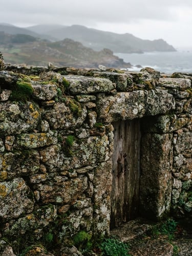 Detalle de la antigua mampostería de granito del Santuario de San Andrés de Teixido, con liquen y musgo, bajo una suave luz atlántica de día nublado, en un encuadre vertical.