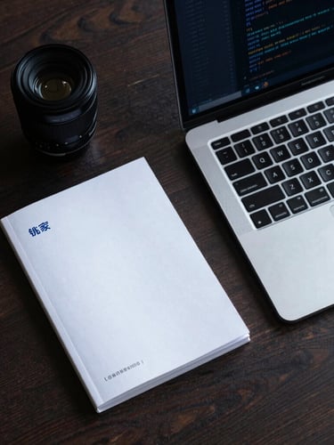 Top-down organized desk layout with a physical brand book next to an open laptop displaying a clean code editor, cold blue highlights, sharp shadows