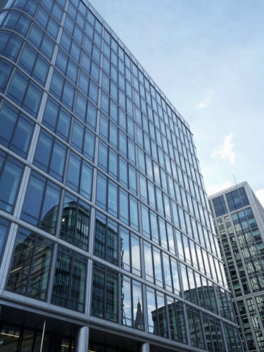 Wide-angle architectural photograph of a modern glass corporate headquarters in London, cool crisp daylight, deep blue reflections, high-end institutional aesthetic