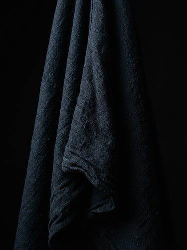 Stark studio photography of heavyweight Japanese cotton fabric drape, dramatic chiaroscuro lighting, deep shadows, high contrast black background, sharp focus, 85mm