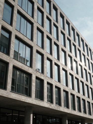 Wide-angle architectural elevation of a modern concrete and glass building facade in Munich, high-contrast cool daylight, sharp geometric shadows, minimalist aesthetic.
