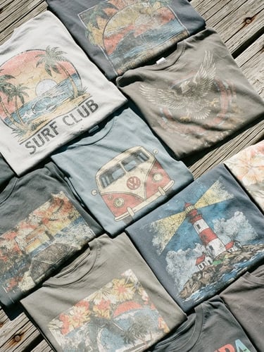 Gritty film photography, top-down flat lay of sun-bleached graphic t-shirts on weathered coastal wooden boards, harsh midday sunlight, high contrast, 35mm
