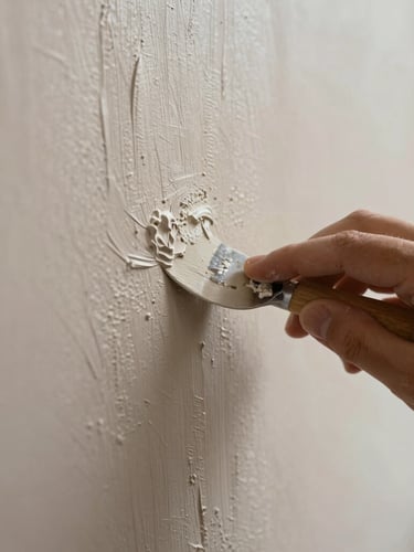 Extreme close-up of a hand applying Venetian plaster to a wall, showing the subtle trowel marks and the developing polished surface. Soft natural light, shallow depth of field, rich tactile texture.