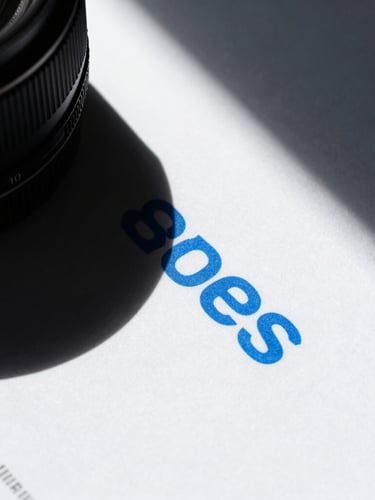 Extreme close-up of a high-contrast printed brand book on heavy textured paper, harsh direct sunlight casting sharp geometric shadows, electric blue ink visible on white paper, 35mm lens.
