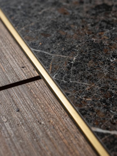Macro architectural photograph of premium materials meeting: dark veined marble joining a weathered teak deck with a razor-thin brass inlay, dramatic side lighting.