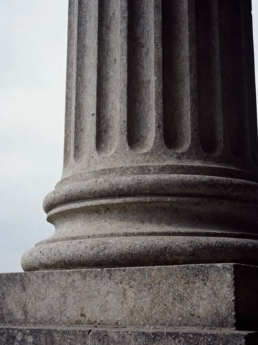 Extreme close-up of a carved stone classical pillar, deep shadows, natural overcast side-lighting, editorial architectural photography, 35mm film